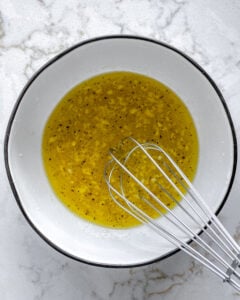 process of whisking lemon dressing ingredients together in white bowl against white background