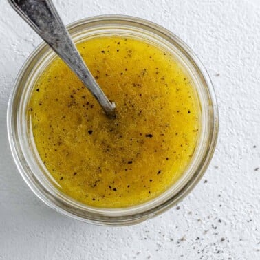 completed lemon dressing in a glass jar with a spoon in it against a white background