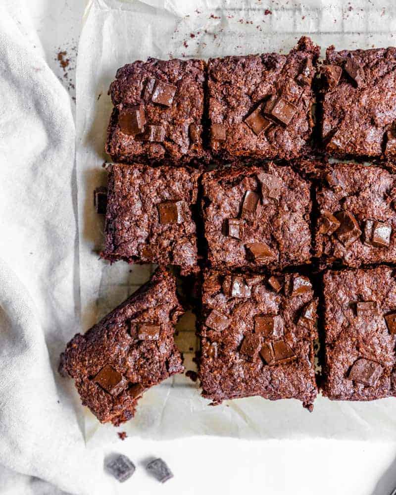 completed vegan Super Fudgy Brownies with a piece cut out on parchment paper