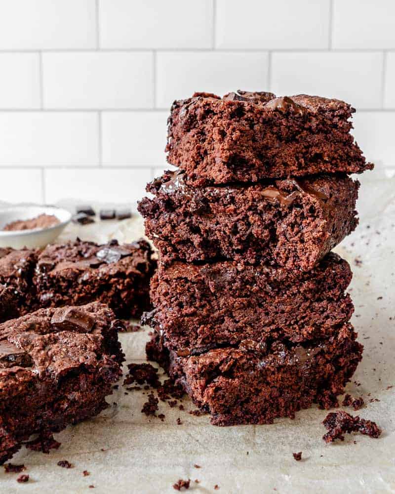 completed Super Fudgy Brownies stacked on each other in squares on parchment paper