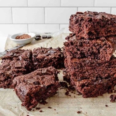 completed Super Fudgy Brownies stacked on each other in squares on parchment paper