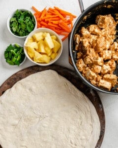 marinated tofu in a bowl alongside separate bowls of veggies and pizza dough