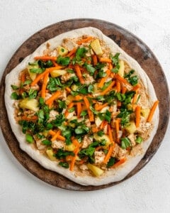 process shot showing pizza toppings now placed on pizza dough against a brown and white surface