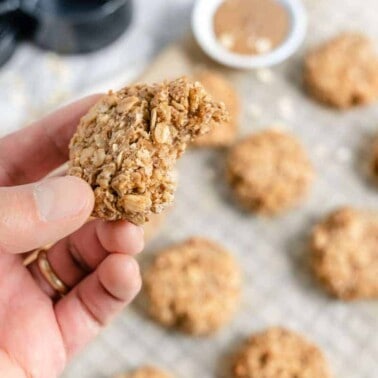 close up of Coconut Oatmeal Cookie with several cookies on a gray baking tray with ingredients in the background