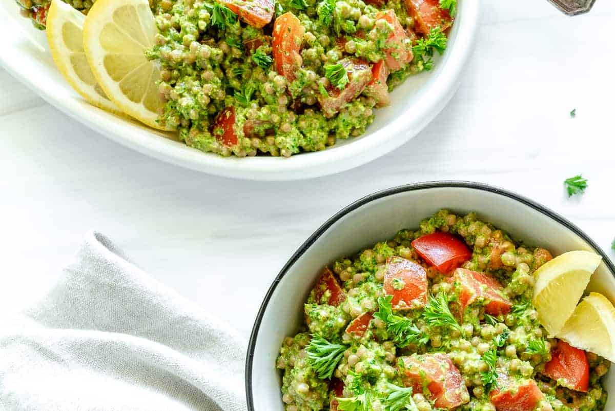 two bowls of arugula pesto couscous in a white platter and bowl against a white background