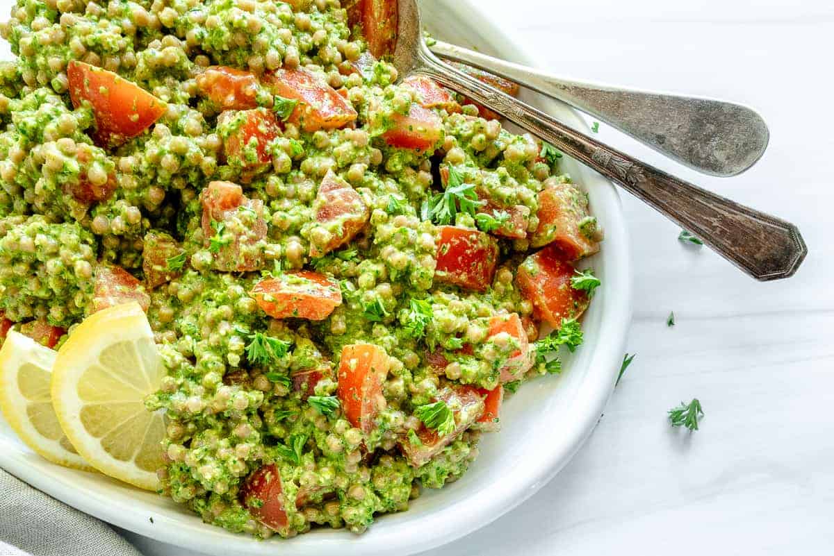 arugula pesto couscous in a white platter against a white background