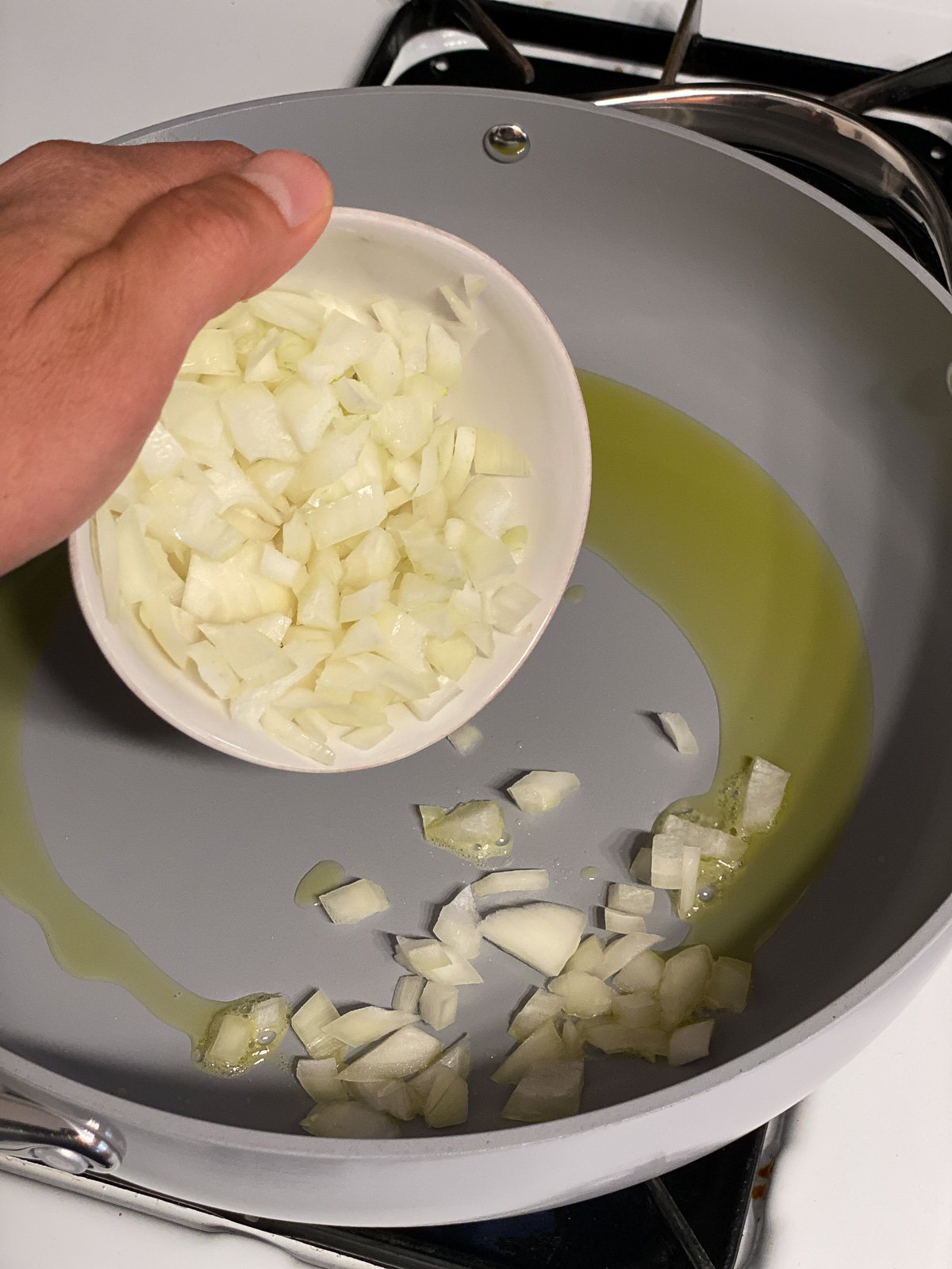process shot of onion being added to gray pan with olive oil
