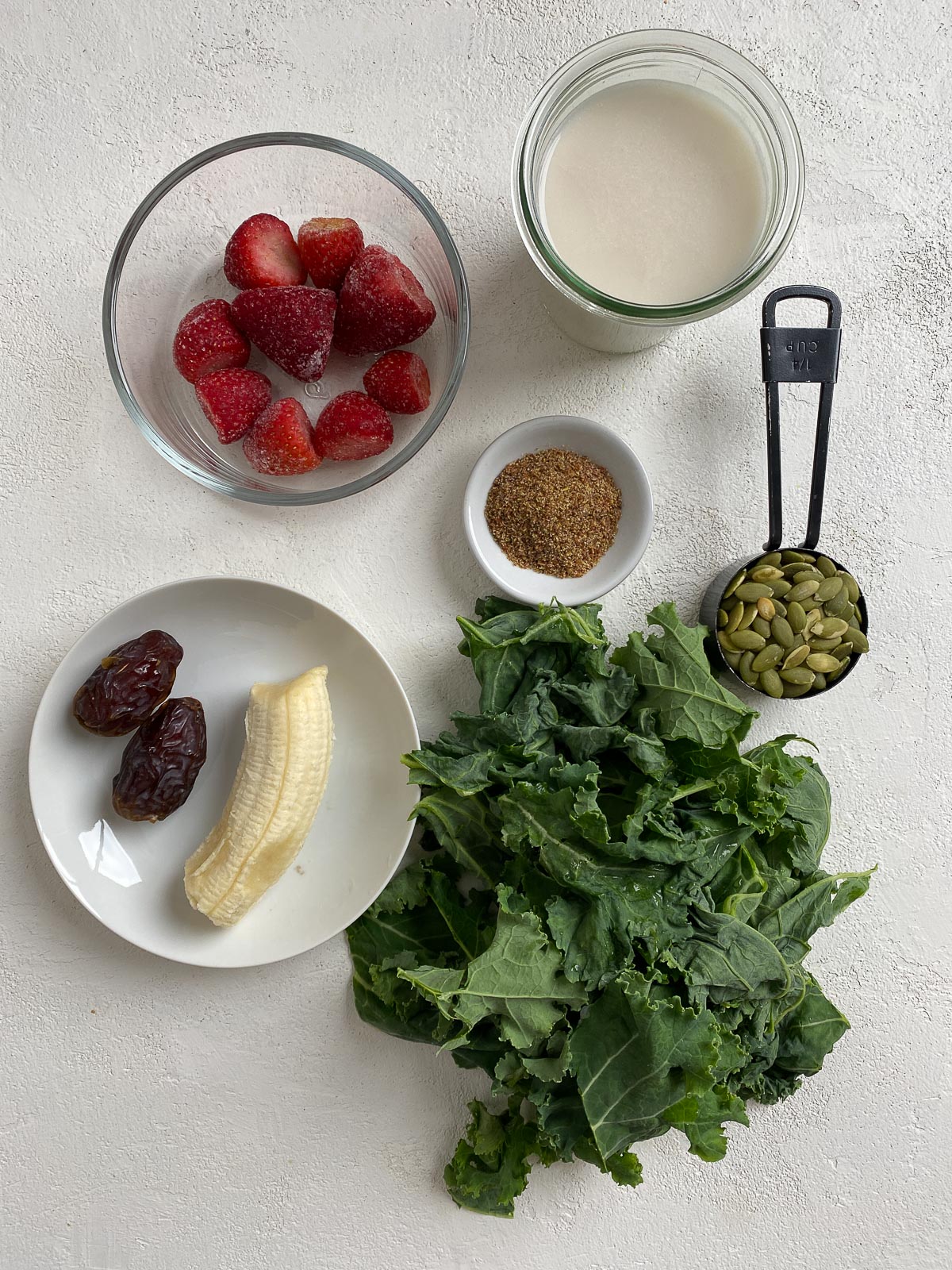 ingredients for Strawberry Kale Smoothie spread out on a white surface