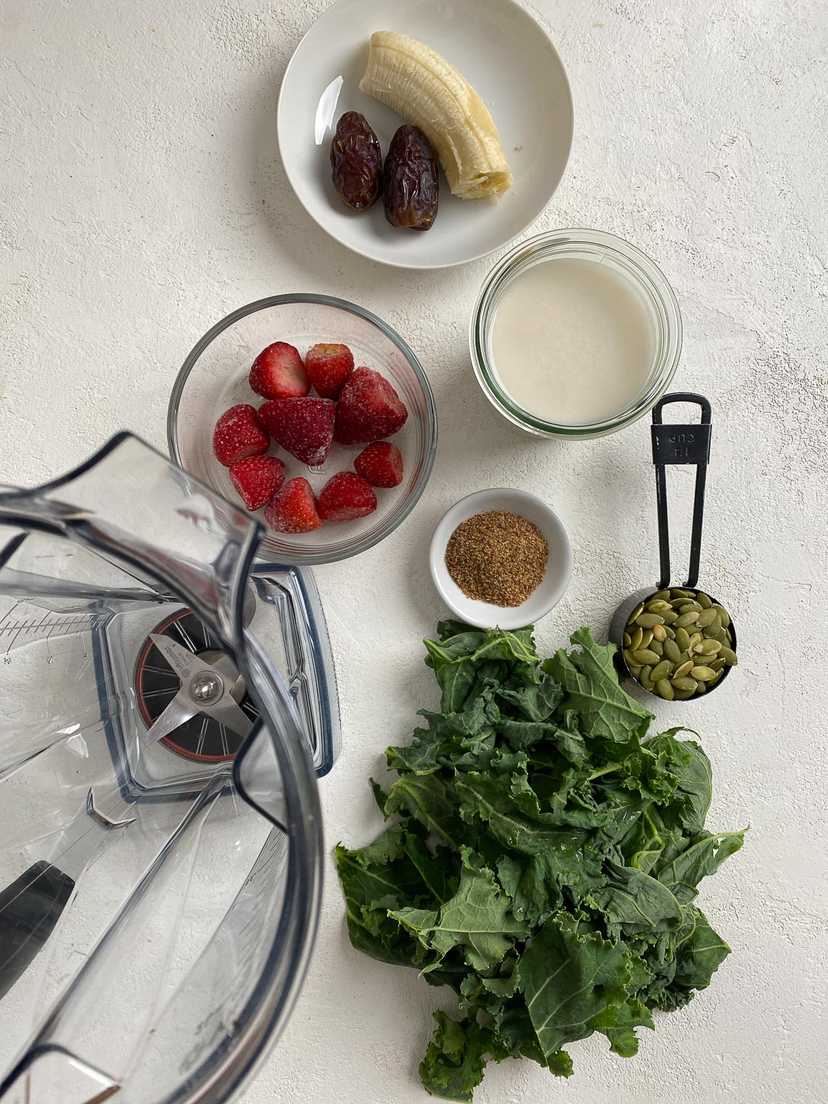 ingredients for Strawberry Kale Smoothie spread out on a white surface alongside a blender