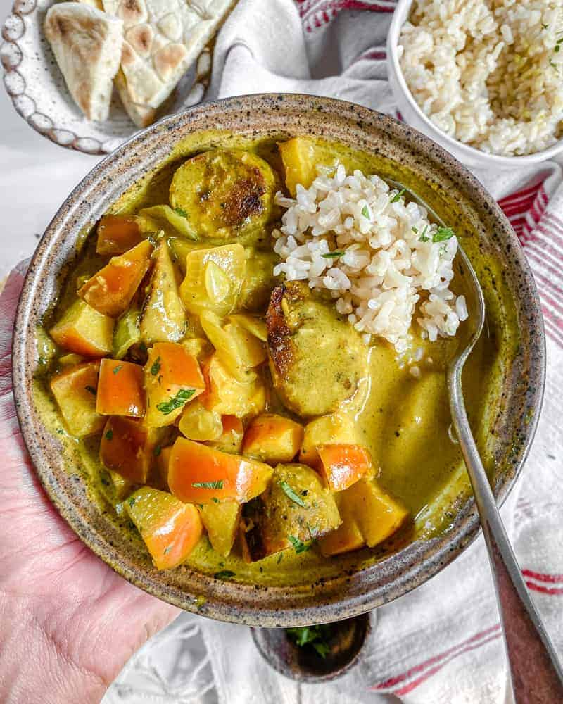 finished Vegan Coconut Curry with Apples in a brown bowl with bread and rice in the background