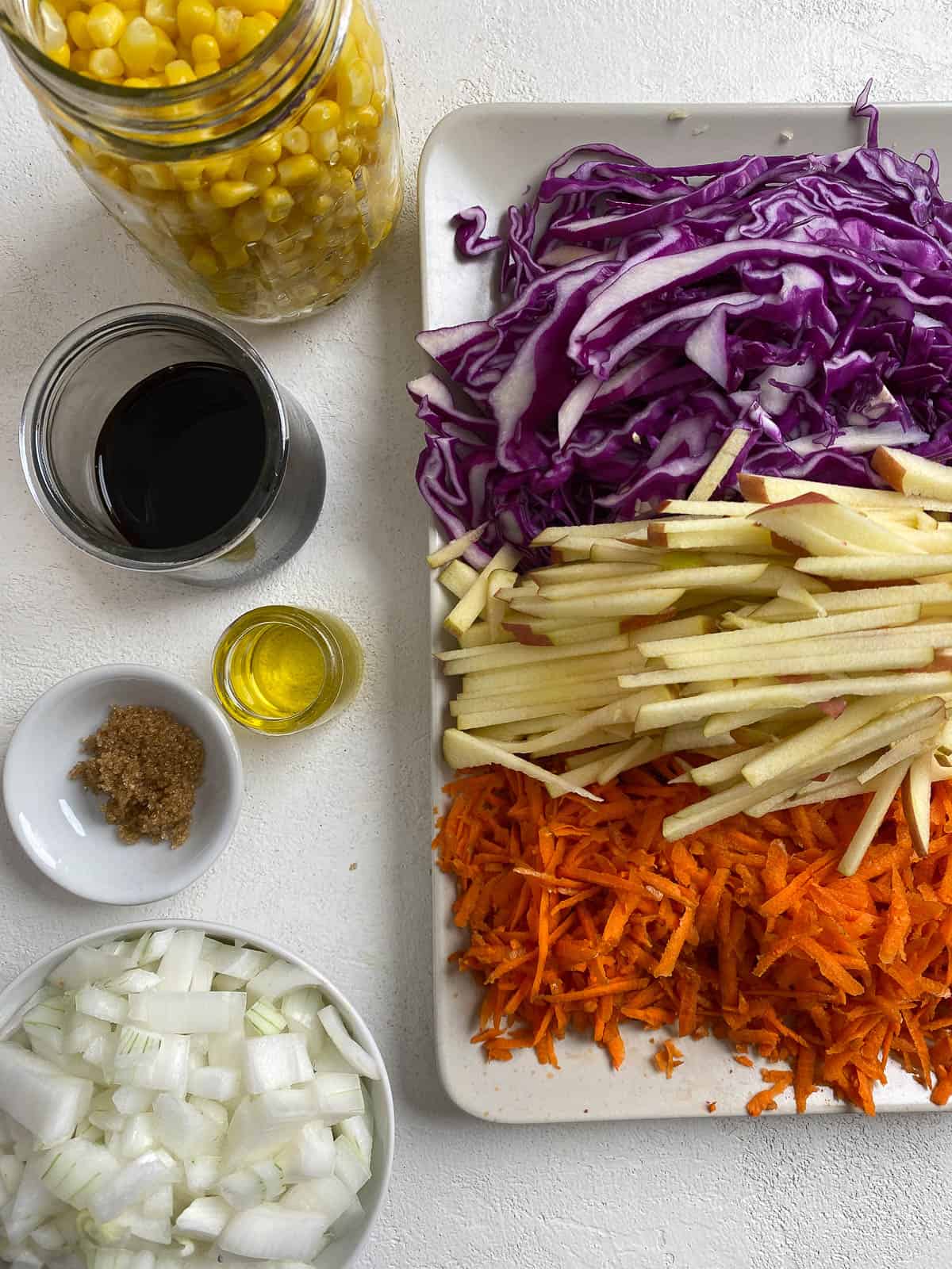ingredients for slaw measured out and veggies cut on a white surface