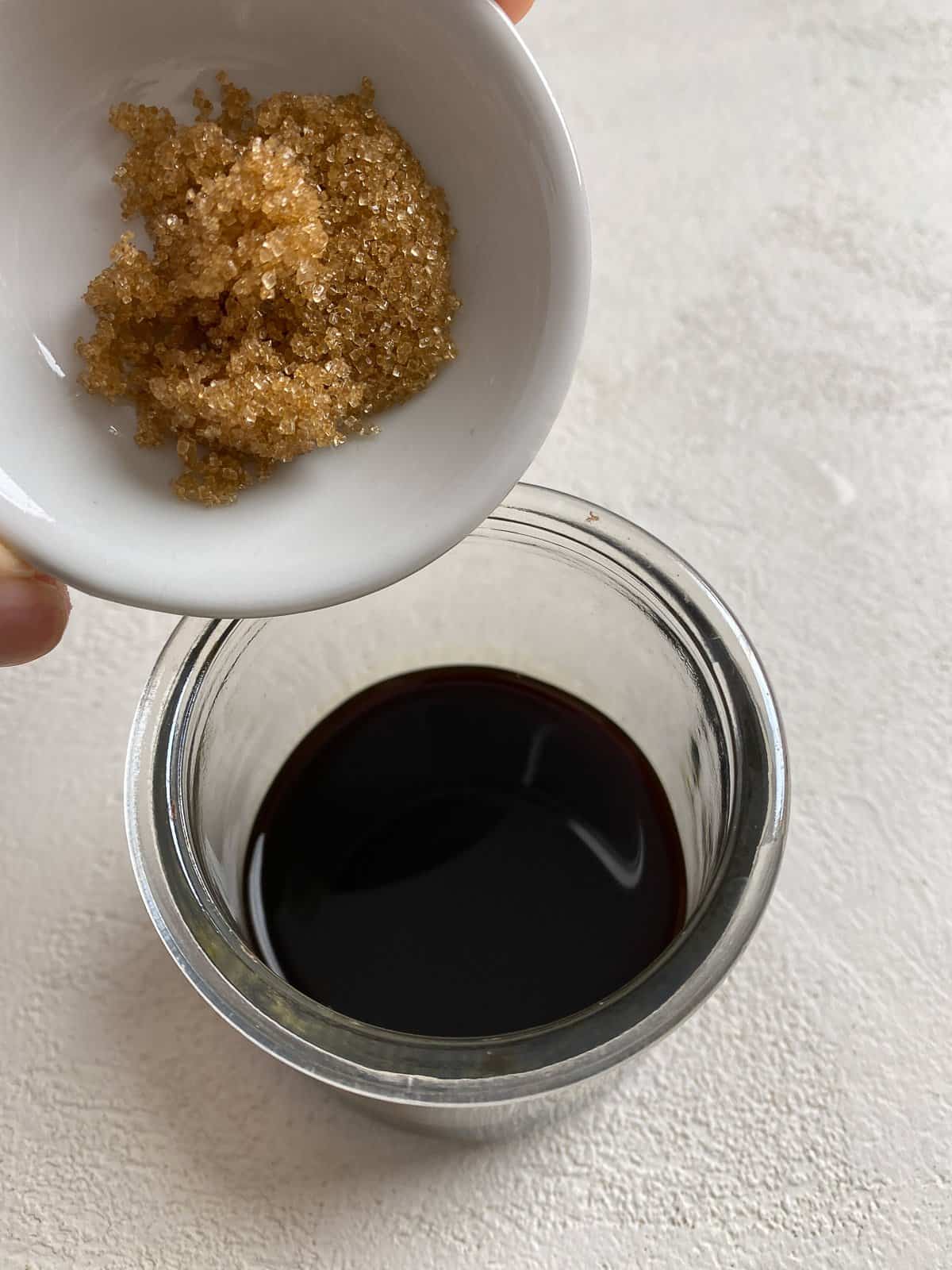process of adding sugar to soy sauce in clear bowl