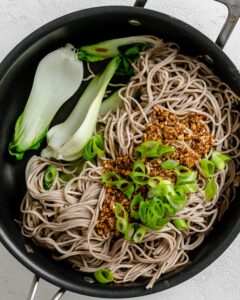 process of adding sauce and veggies to pan of noodles