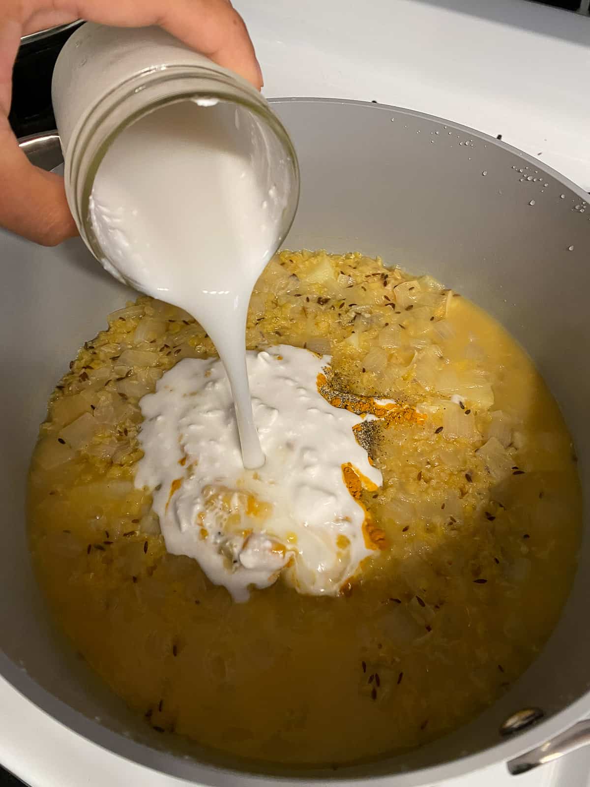 process shot of adding canned coconut milk to pan