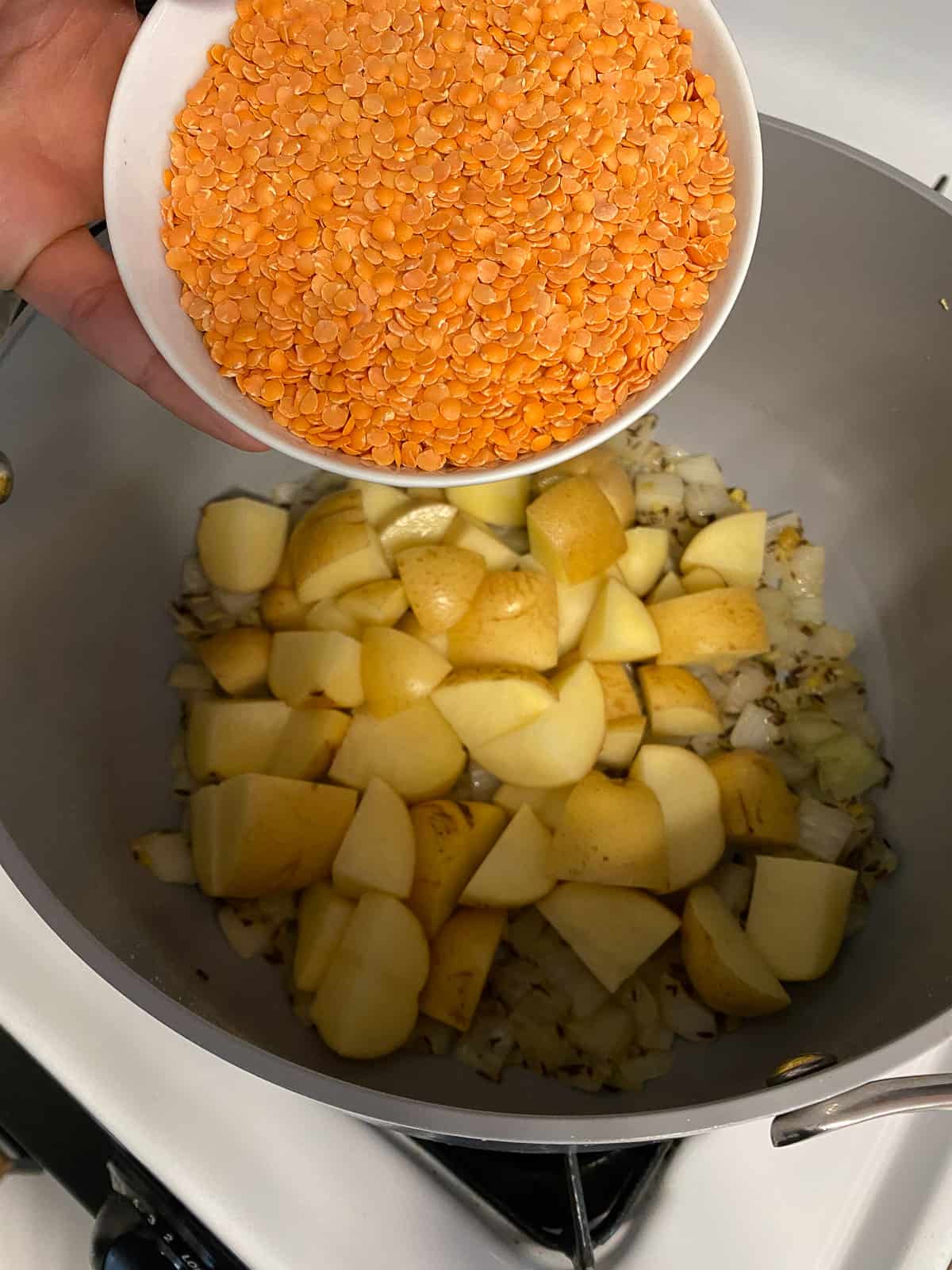 process shot of red lentils being added to pan