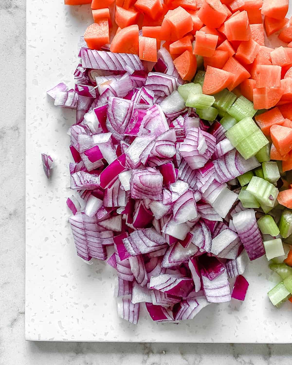 ingredients for mirepoix diced on a white cutting board