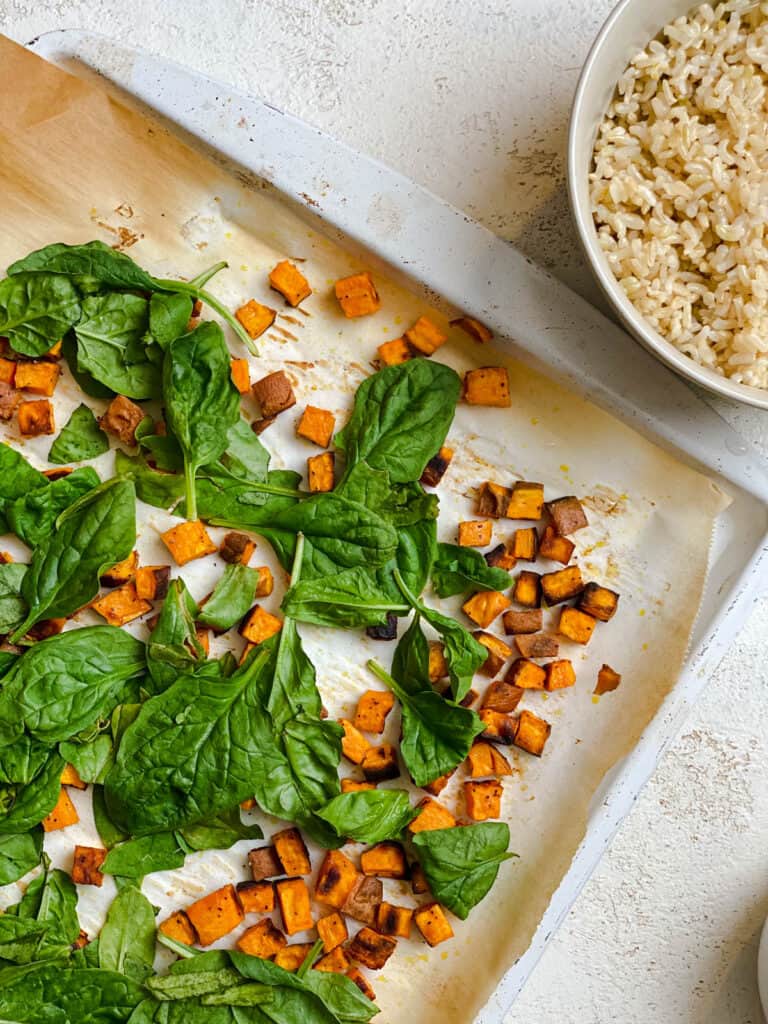 post baked spinach and sweet potatoes in baking tray alongside bowl of rice