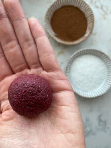 rolled beet energy ball in palm of hand with ingredients in the background