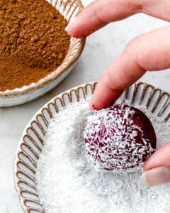 process of coating beet energy ball in shredded coconut in a bowl