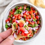 completed Pico de Gallo in a white bowl with a close up of a chip dipped in it