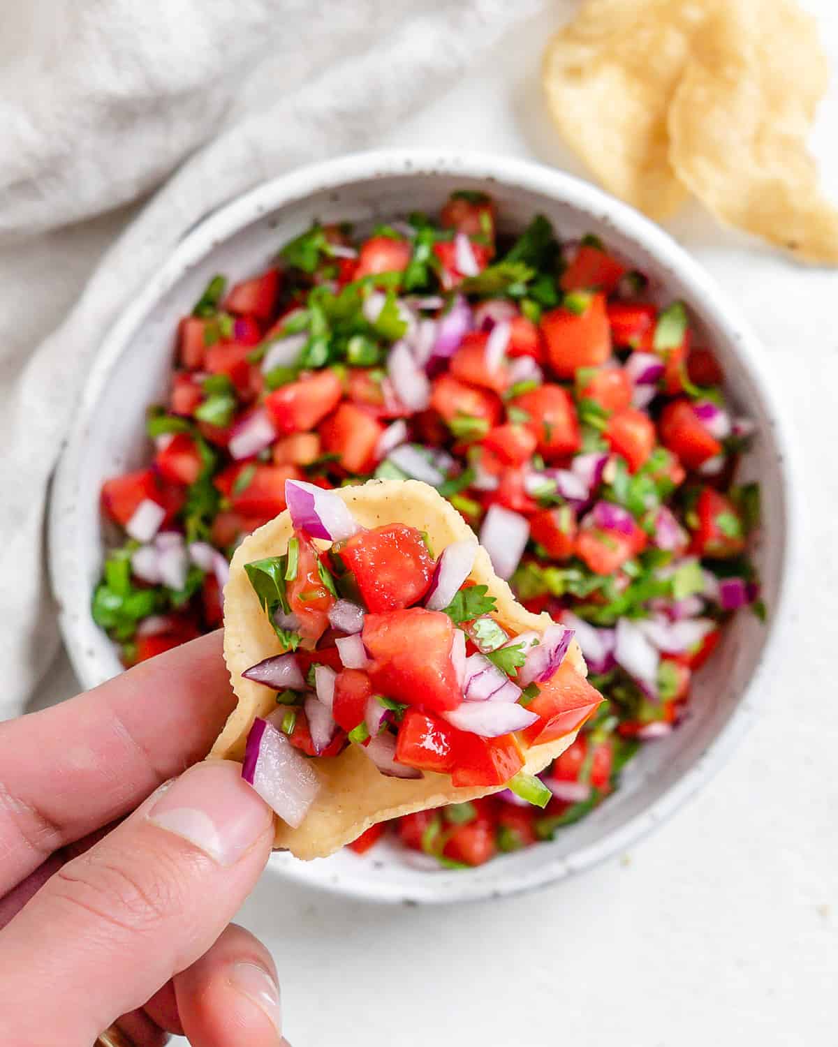 completed Pico de Gallo in a white bowl with a close up of a chip dipped in it