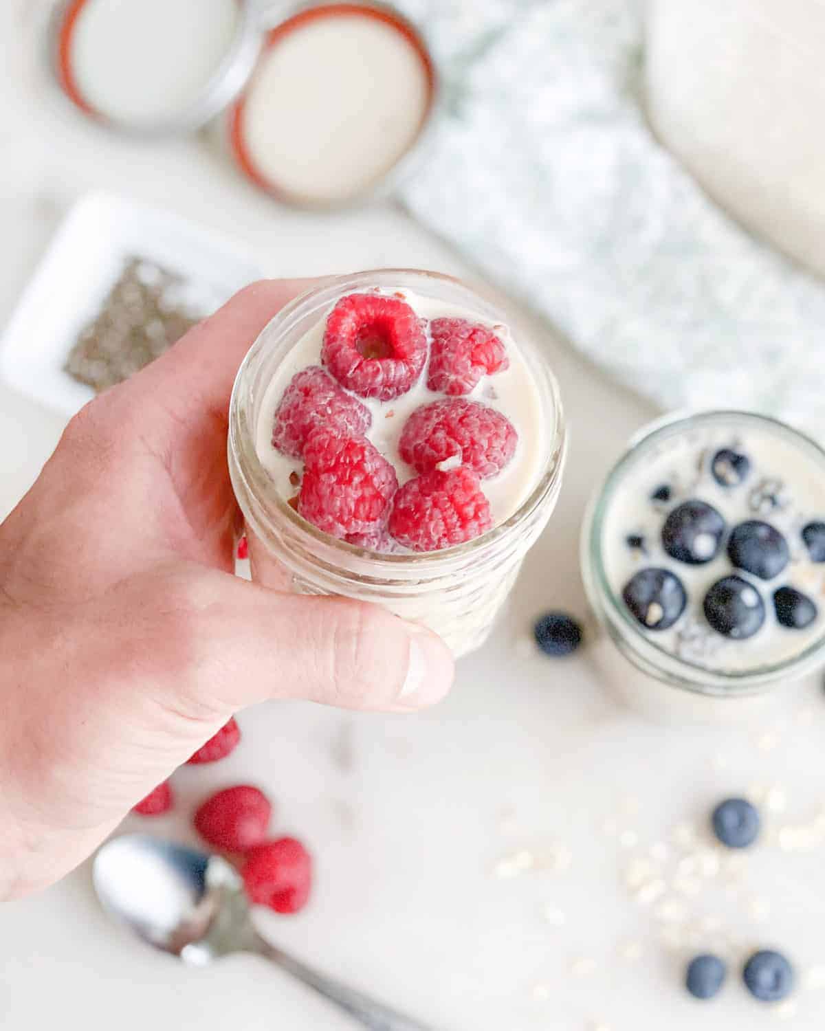 close up of overnight oats with raspberries and blueberries on top against a light surface