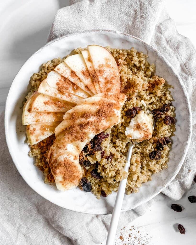 completed Breakfast Quinoa Apple Bowl in a white bowl with ingredients scattered in the background