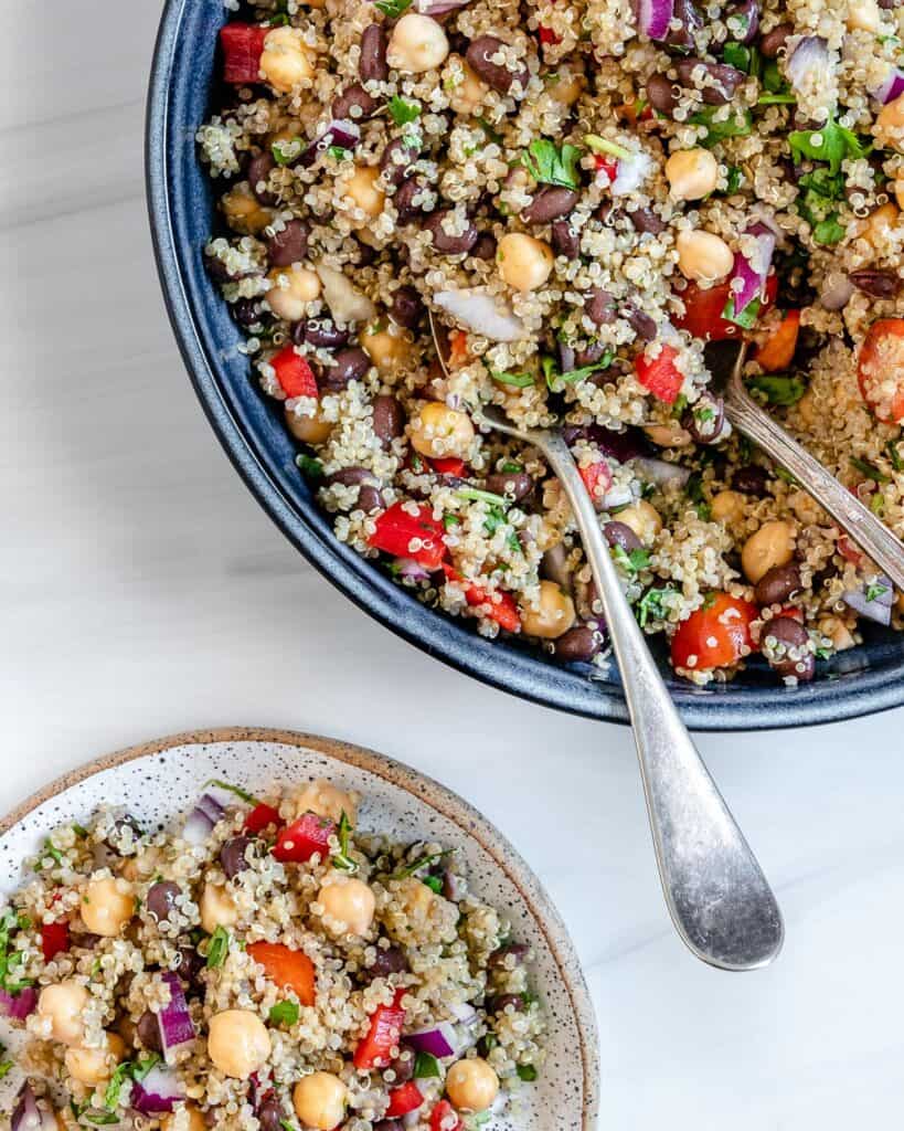 completed Fresh Quinoa Salad in a blue bowl with utensils against a white background