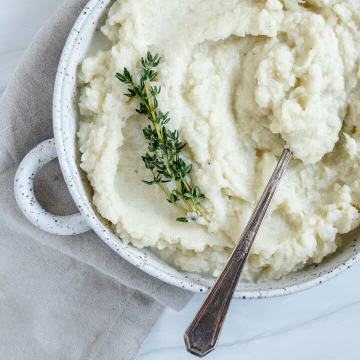 completed mashed cauliflower in a white dish with a spoon in the mashed cauliflower against white background