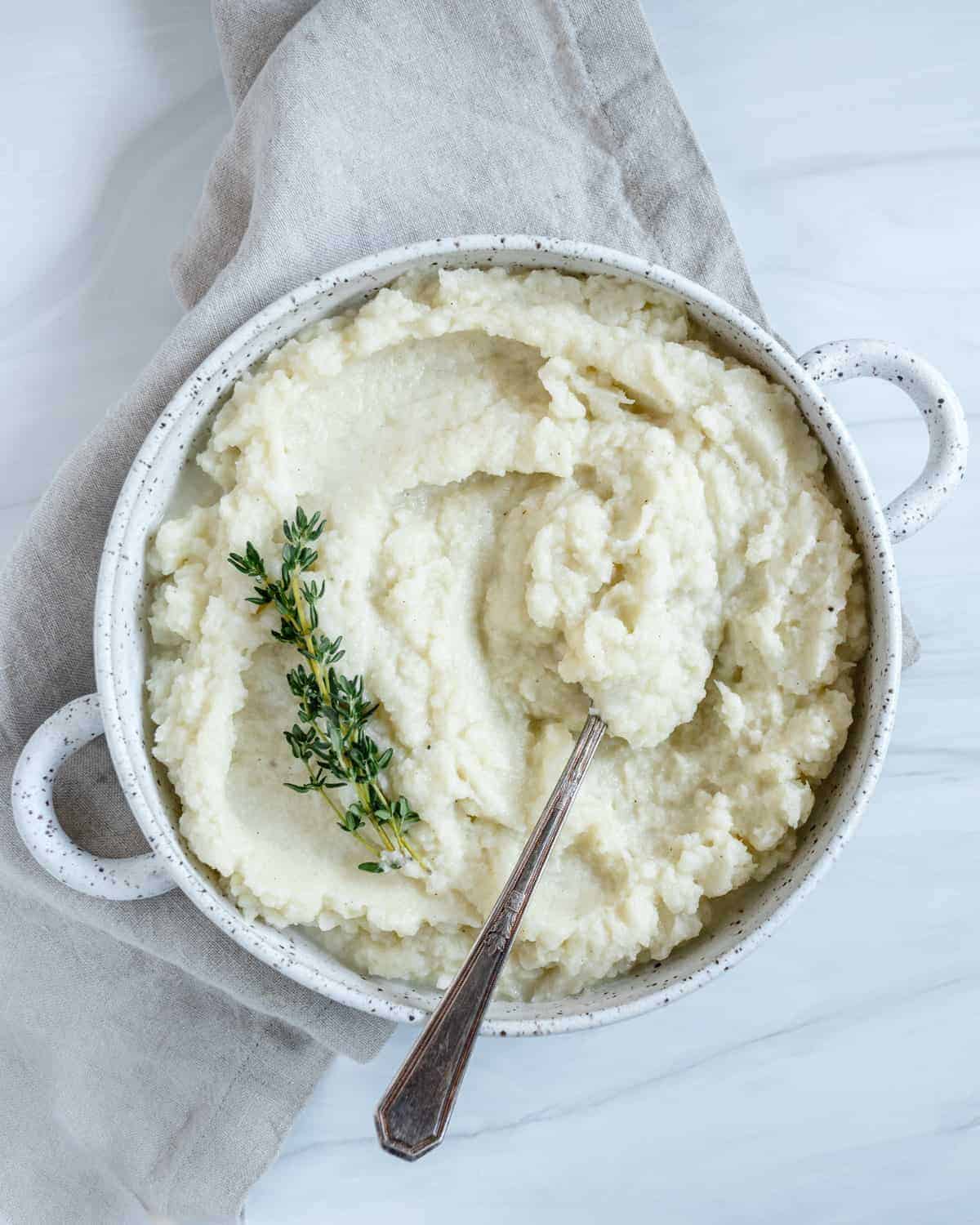 Creamy vegan mashed cauliflower in a white bowl with a spoon.