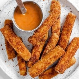 completed vegan breaded tofu strips on a white plate with a small bowl of sauce on the plate