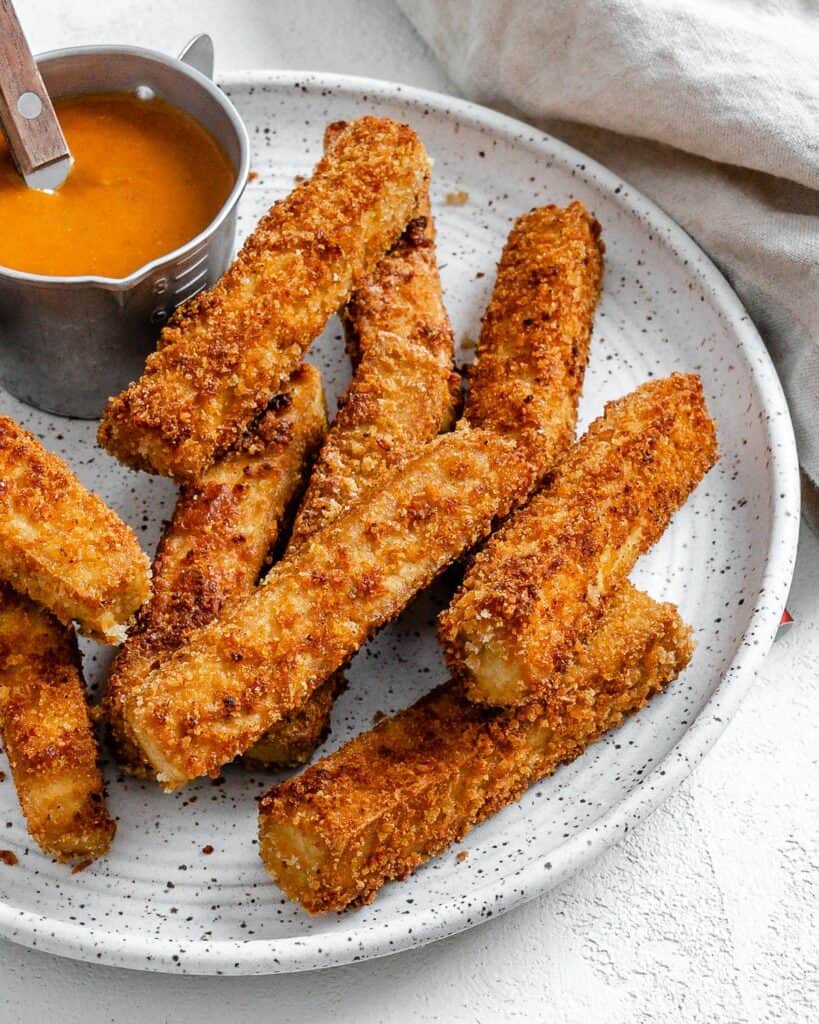 completed vegan breaded tofu strips on a white plate with a small bowl of sauce on the plate