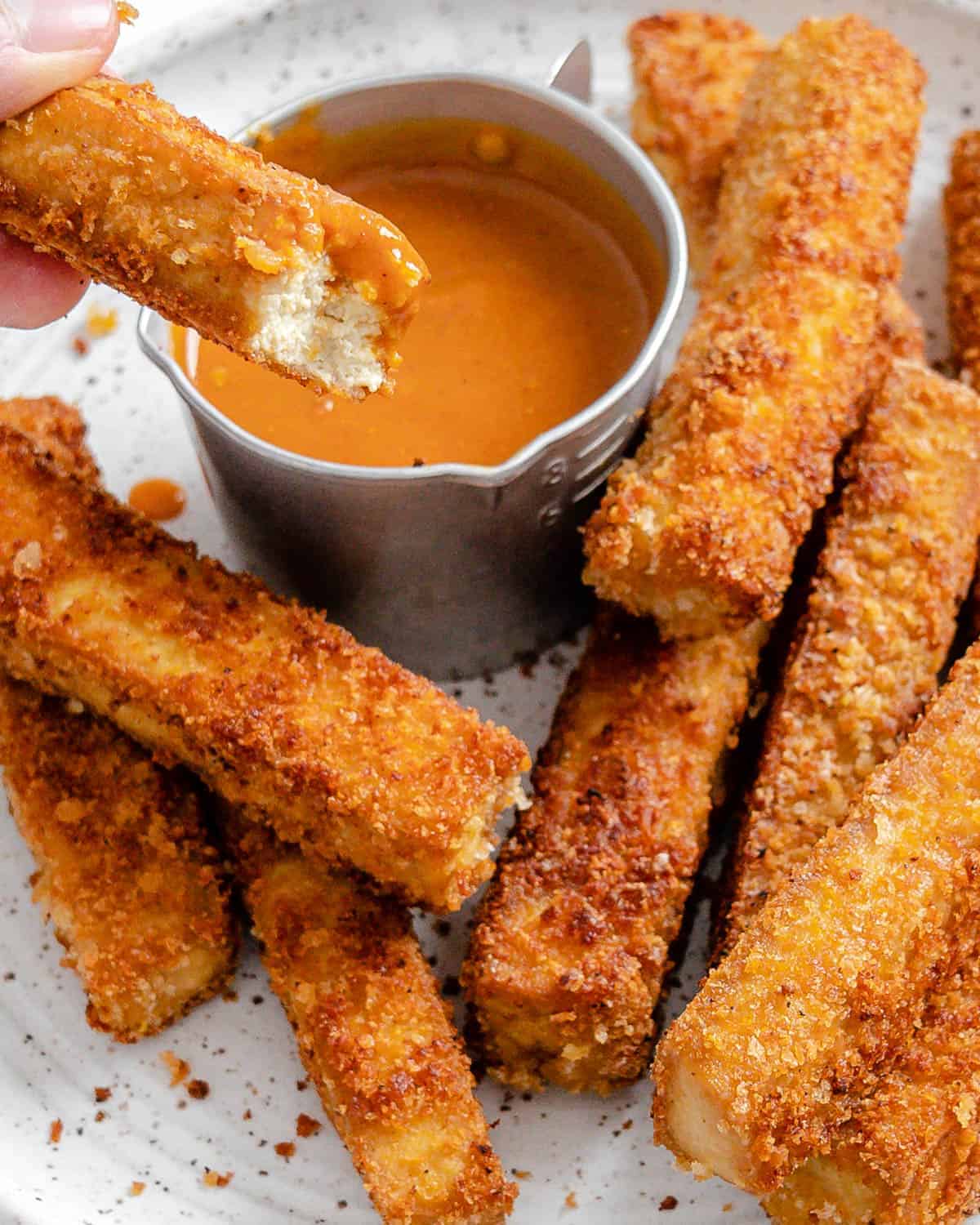 completed vegan breaded tofu strips on a white plate with a small bowl of sauce on the plate