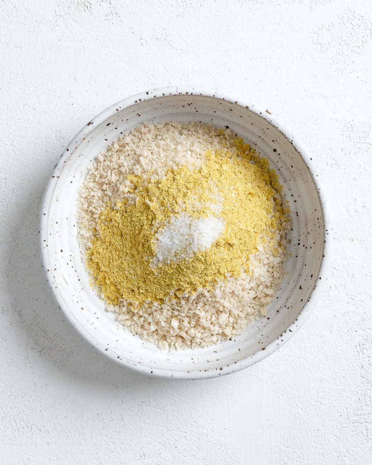 process of mixing breaded ingredients into white bowl against white background
