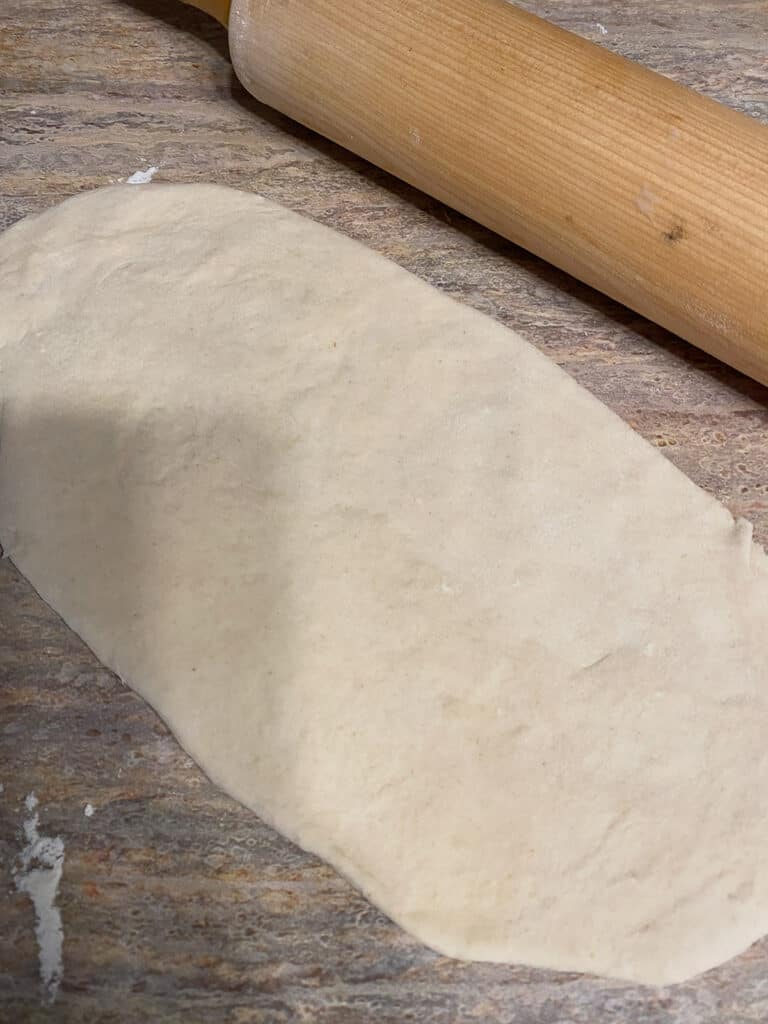process shot of flattening out Cinnamon Roll dough against brown surface