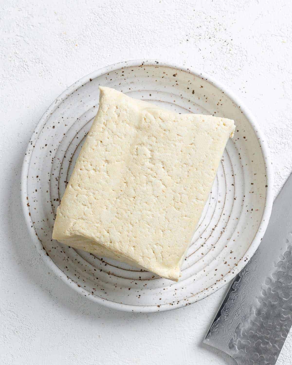 block of tofu on a small white plate against a white surface
