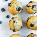 completed blueberry muffins on a white surface with blueberries scattered in the background