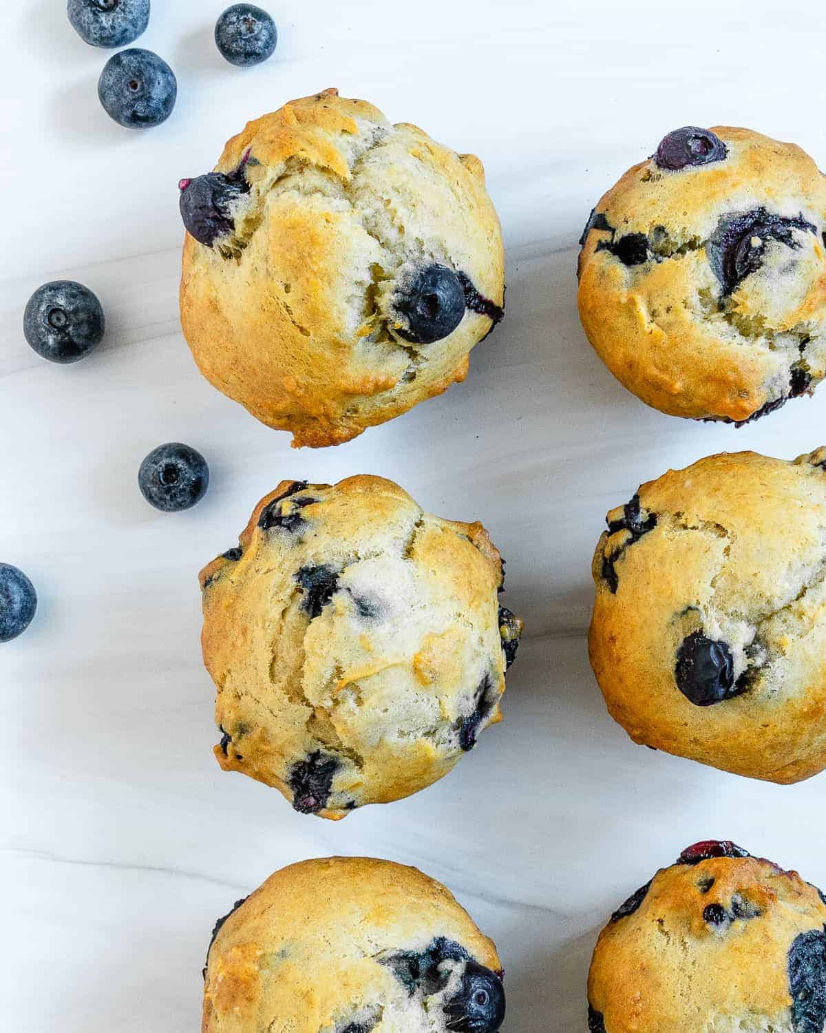 completed blueberry muffins on a white surface with blueberries scattered in the background