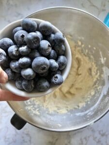 process of adding bowl of blueberries to batter