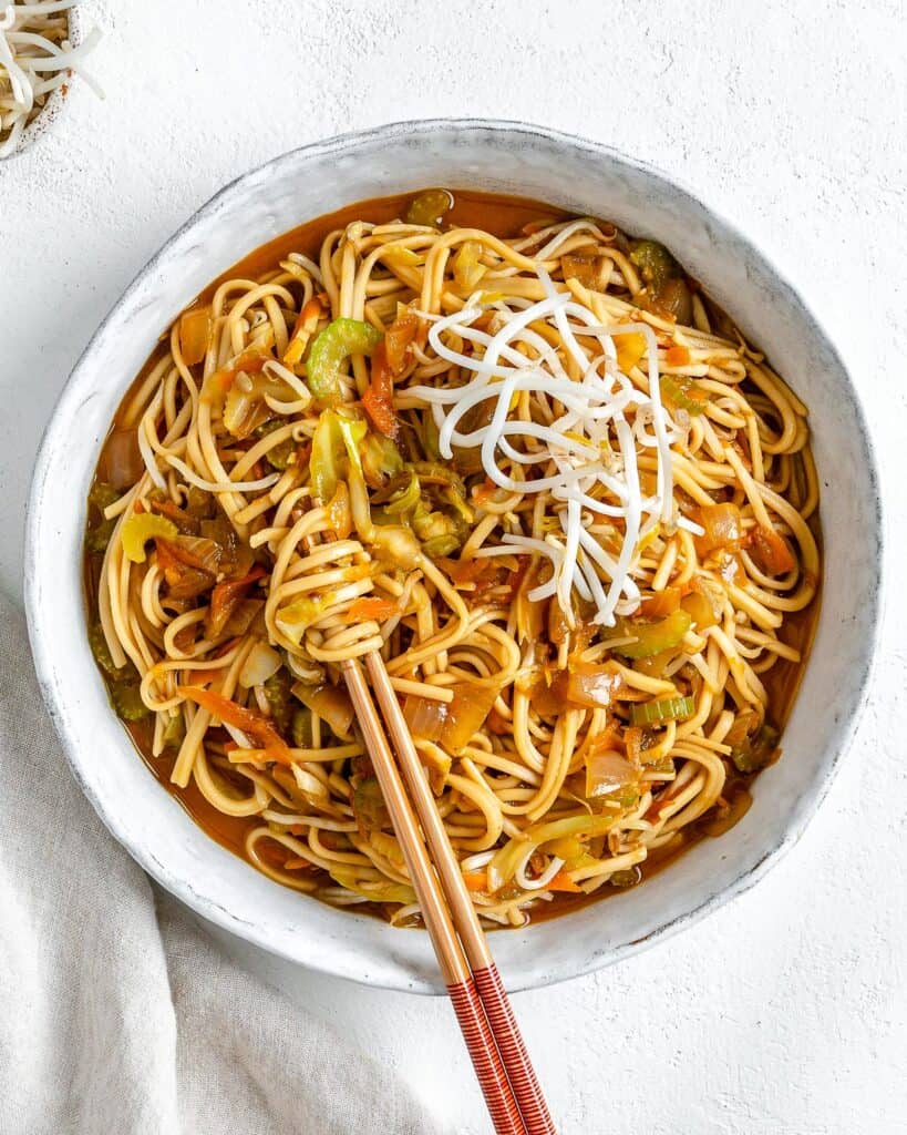 completed bowl of Veggie Chow Mein in a white bowl against a white background with two chopsticks in the bowl