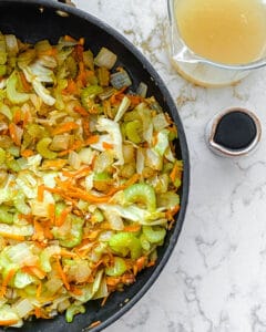process of veggies being cooked in black pan with sauce ingredients on the side against a white background