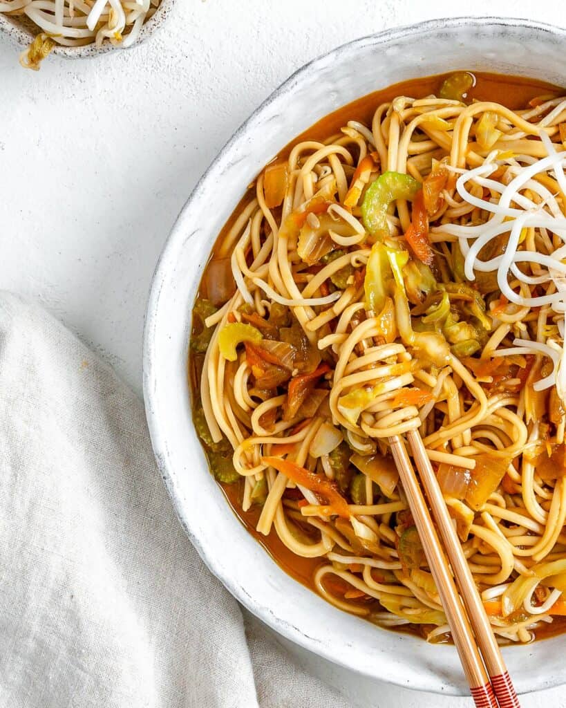 completed bowl of Veggie Chow Mein in a white bowl against a white background with two chopsticks in the bowl
