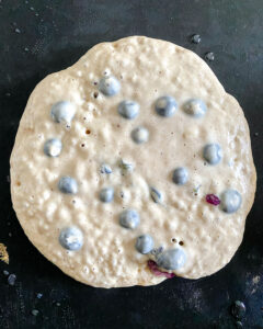 process of making blueberry pancakes with the surface showing bubbles on the griddle