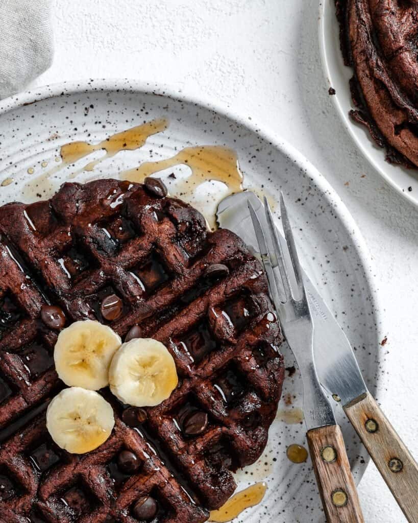 completed waffle on a white plate against a white background with syrup scattered on waffle