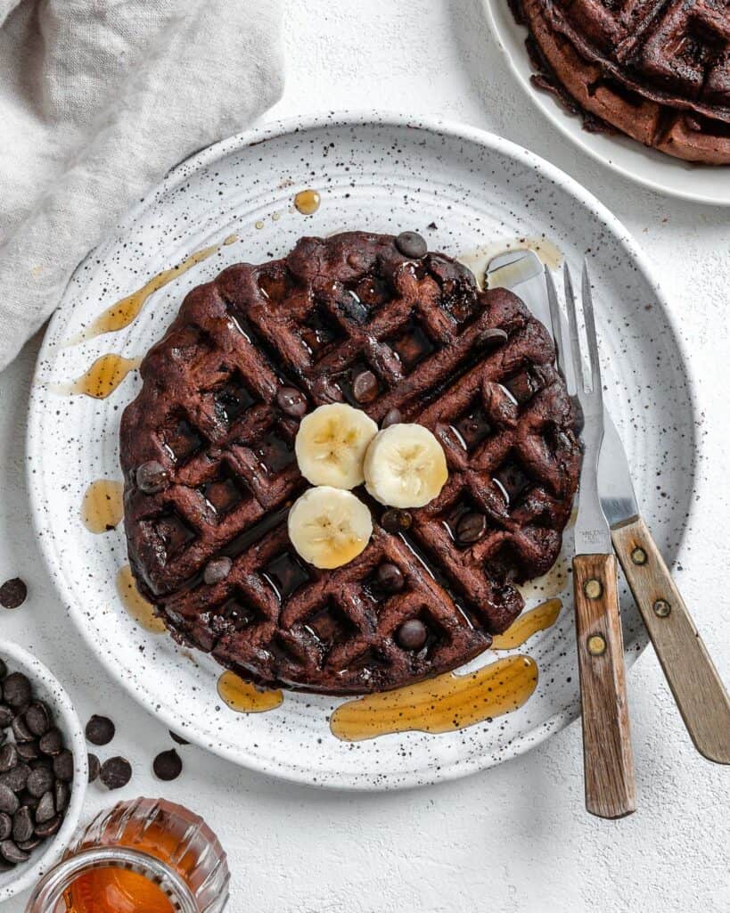 completed waffle on a white plate against a white background with syrup scattered on waffle