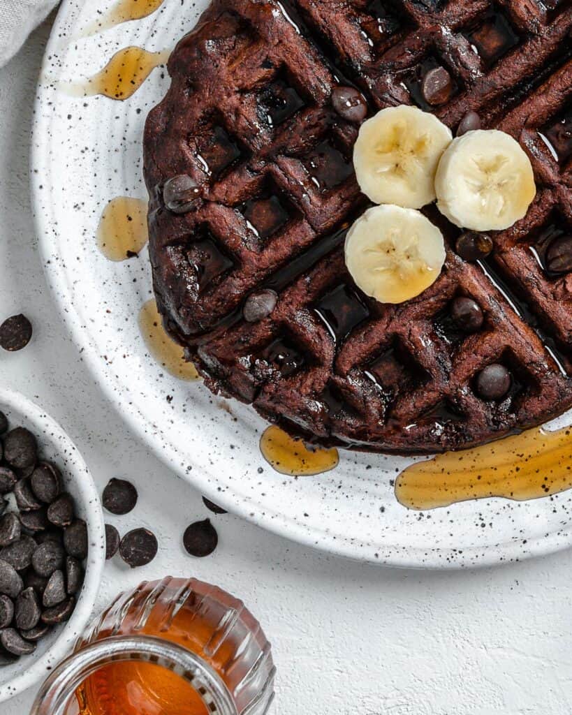 completed waffle on a white plate against a white background with syrup scattered on waffle