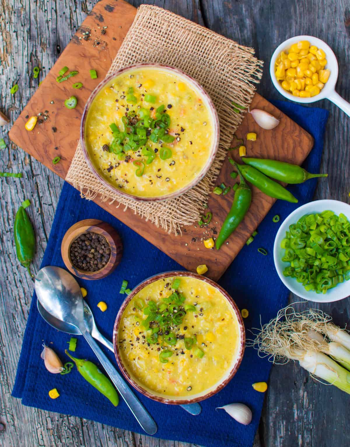 completed Creamy Corn Chowder in two bowls against a blue place mat with ingredients scattered