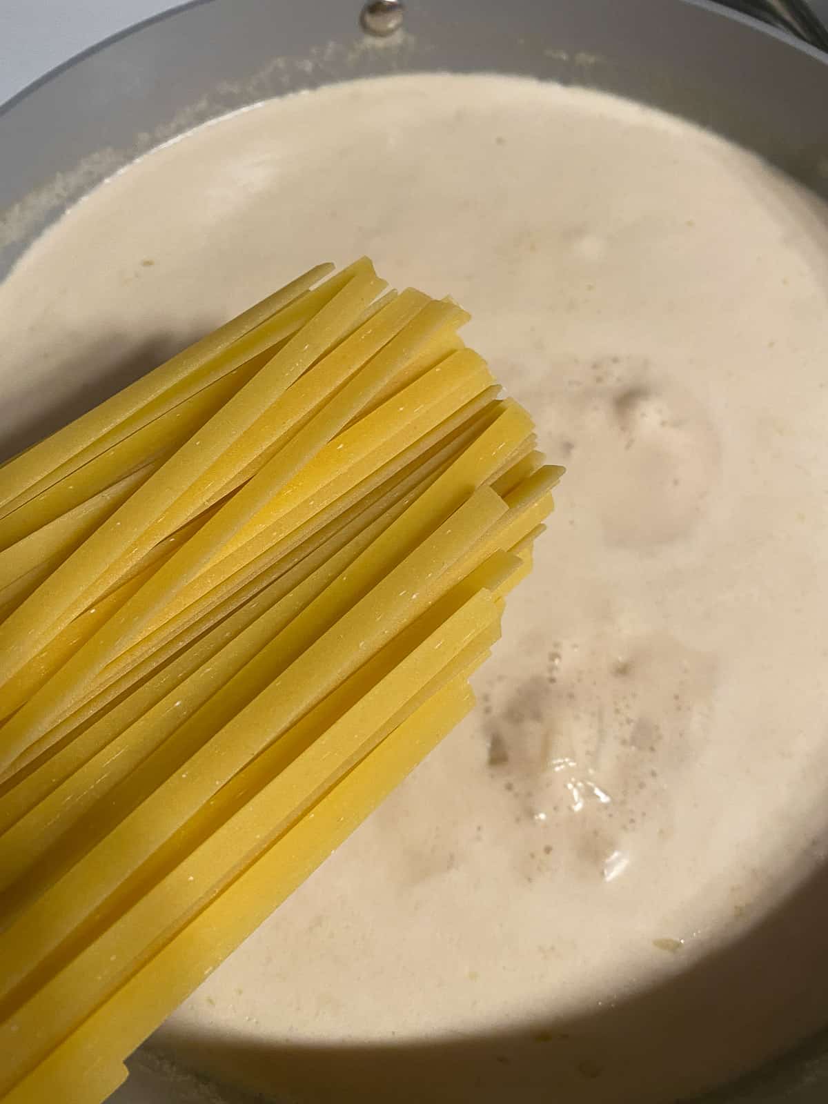 process of adding fettuccine noodles to pan