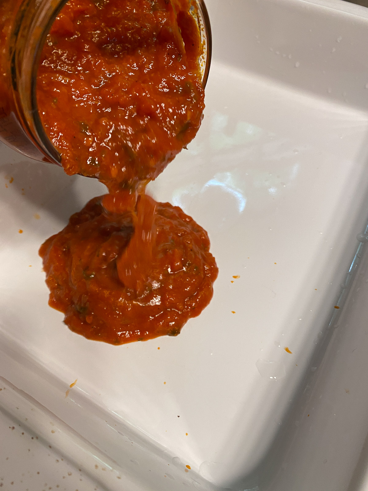 process of spreading marinara sauce in white dish