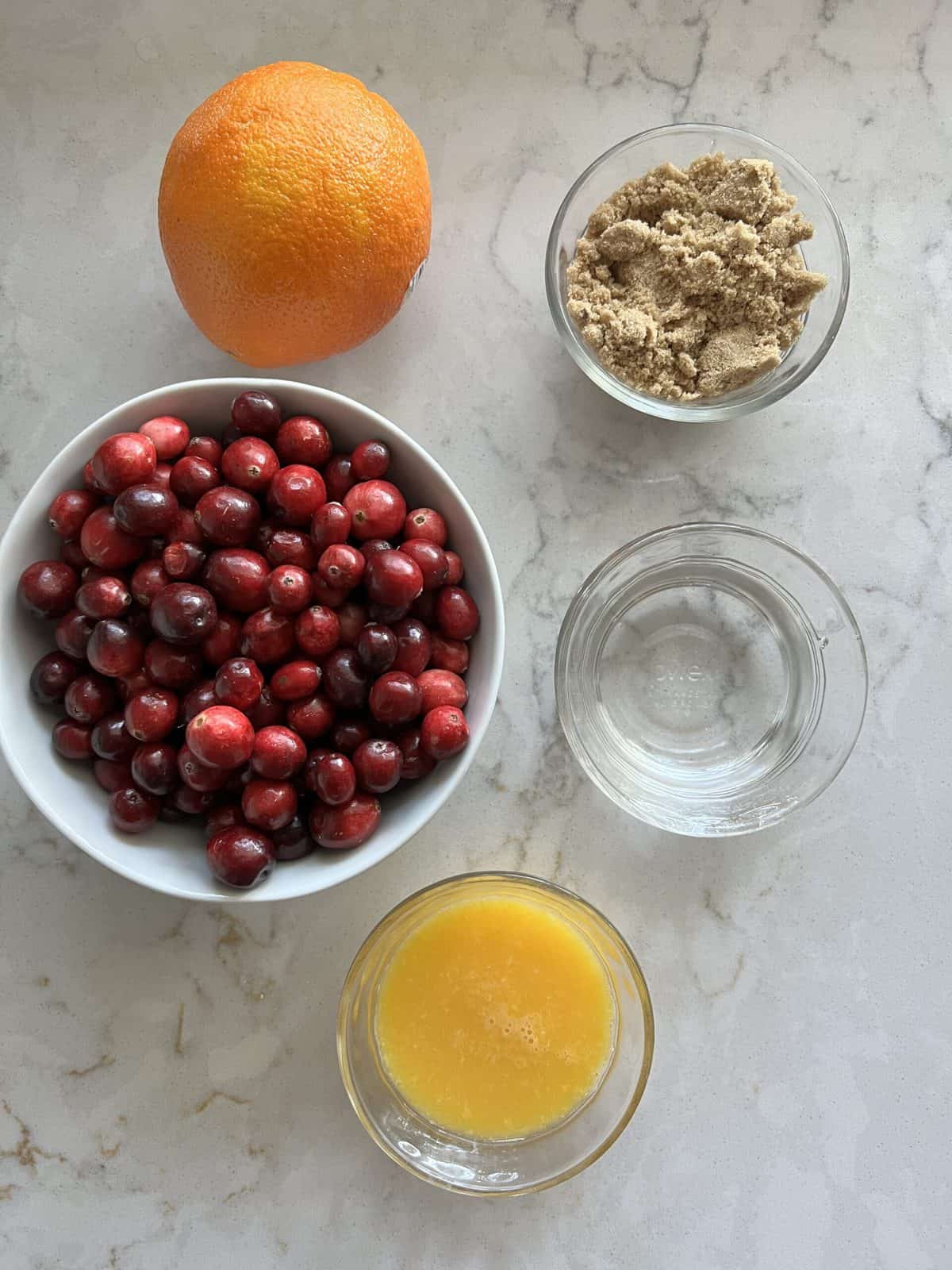 ingredients for Homemade Cranberry Sauce measured out against white marble surface